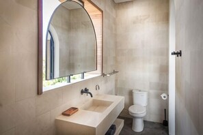 A modern bathroom with a large sink, a toilet, and a mirror with an arched top. - Samastiti Bingin Luxury appartements steps from the beach (Bali)