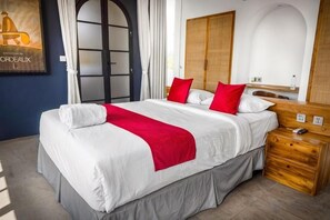 Habitación de hotel con una cama grande, una mesita de noche de madera, un espejo y una puerta con panel de vidrio.