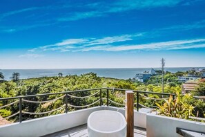 Un balcón con vista al mar y al follaje.