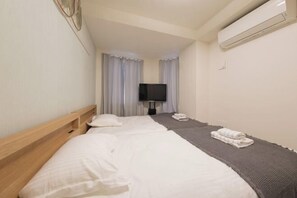 Une chambre d’hôtel avec deux lits, un téléviseur à écran plat, un climatiseur fixé au mur et une fenêtre avec des rideaux.