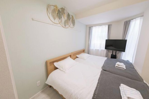 A hotel room with a bed, a flat-screen TV, and a window with curtains. - Sumire 102 (Tokyo)