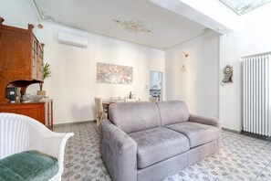 A living room with a grey sofa, a white chair, a wooden cabinet, a painting, and a radiator. - Oasis in the Center of Bologna (Bologna)