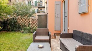 Eine Terrasse mit Korbmöbeln, einem kleinen Tisch und Blick auf ein Gebäude im Hintergrund.