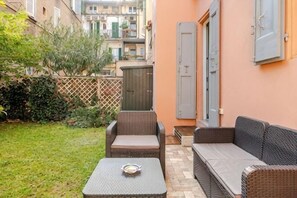 A patio with wicker furniture, a small table, and a view of a building in the background. - Oasis in the Center of Bologna (Bologna)