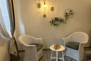 A room with two white wicker chairs with green cushions, a small round table, and wall-mounted decor including a light fixture and a shelf with plants. - Oasis in the Center of Bologna (Bologna)