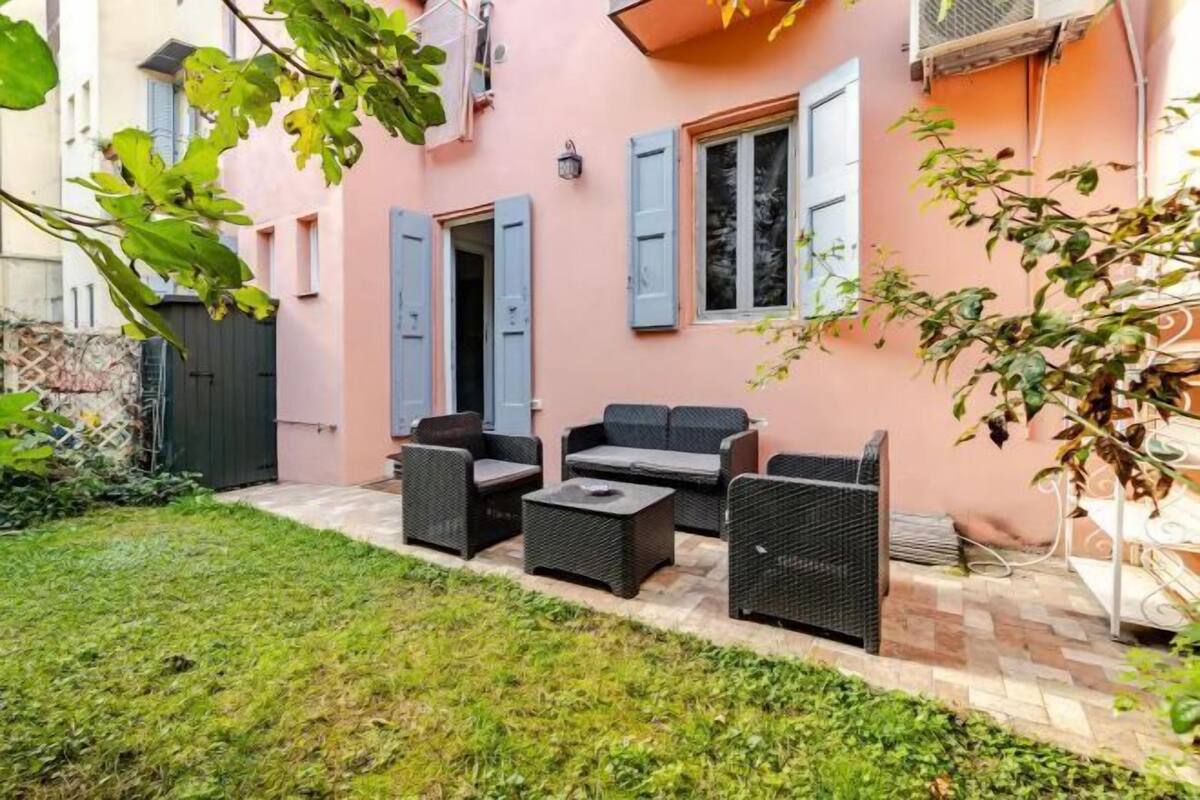 A pink building with a patio area featuring wicker furniture and a tiled floor.