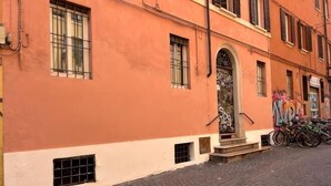 Ein Gebäude mit roter Fassade, einem zentralen Eingang mit einer Tür und einer Treppe, die zum Eingang führt. Das Gebäude hat Fenster und ein Fahrrad steht davor geparkt.