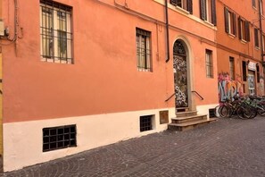 A building with a red facade, a central entrance with a door, and a staircase leading up to the entrance. There are windows on the building, and a bicycle is parked outside. - Oasis in the Center of Bologna (Bologna)