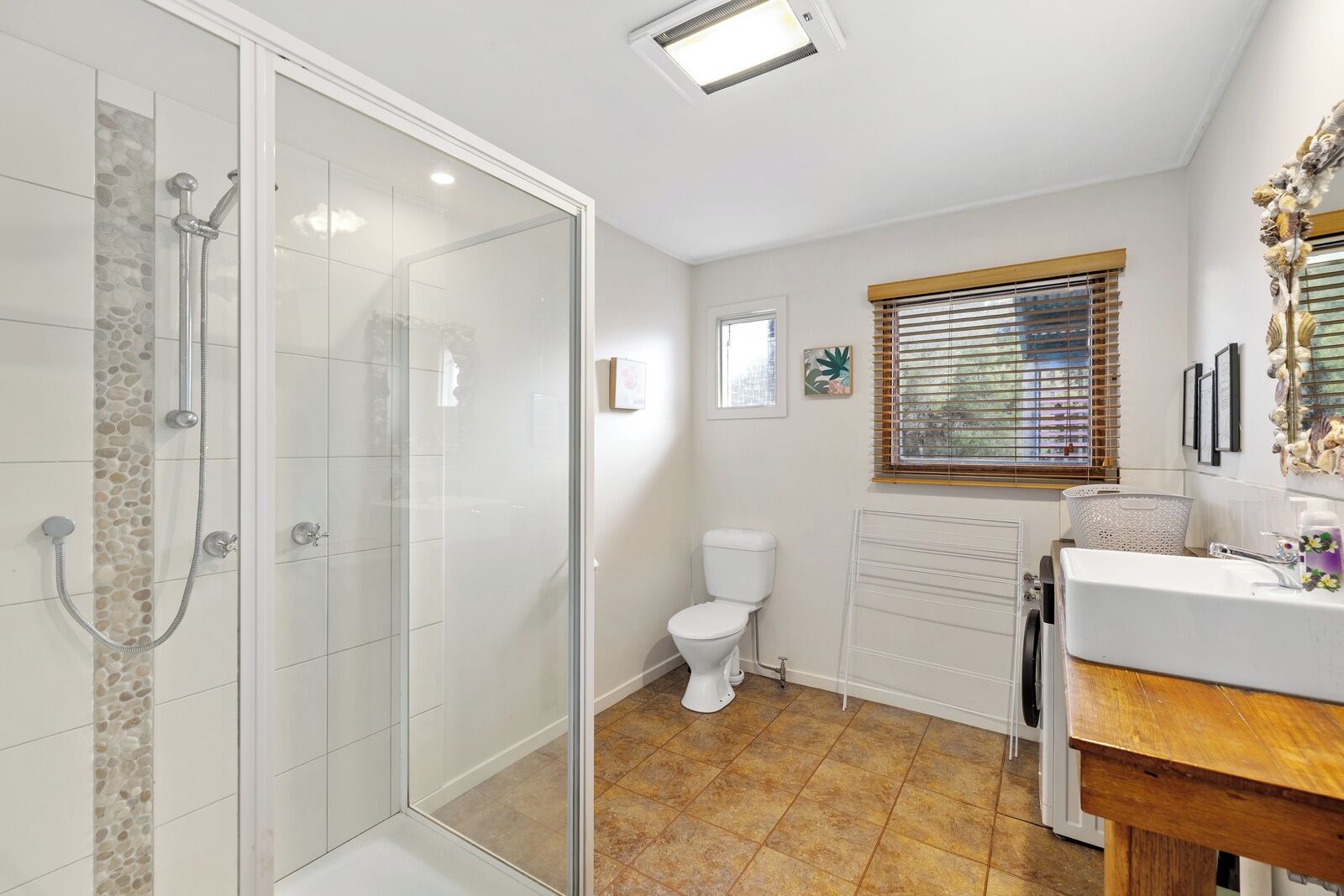 Un baño con ducha envuelta en cristal, inodoro, lavabo y ventana con persianas.