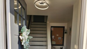 Una escalera que lleva a un rellano con una puerta a la izquierda, un tablón de anuncios y una pequeña mesa con una lámpara.