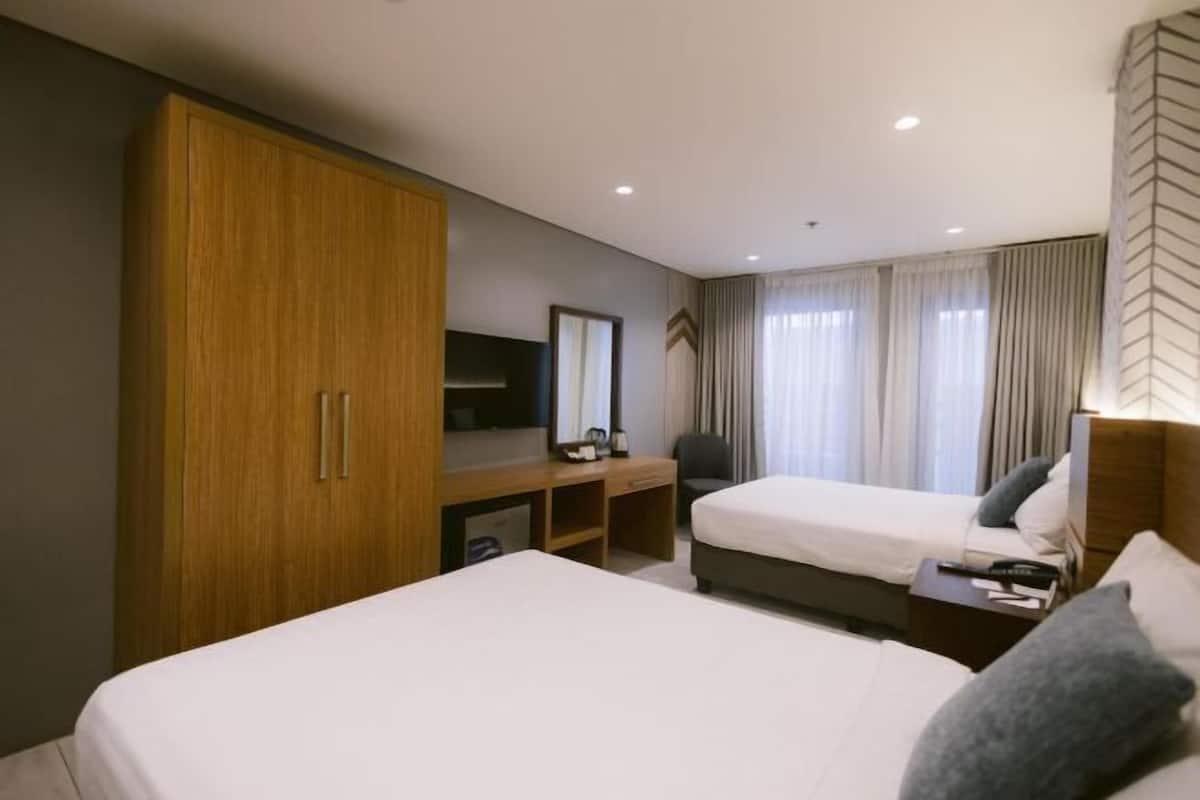 Une chambre d’hôtel avec deux lits, une armoire en bois, un bureau avec un téléviseur à écran plat et une grande fenêtre avec des rideaux.