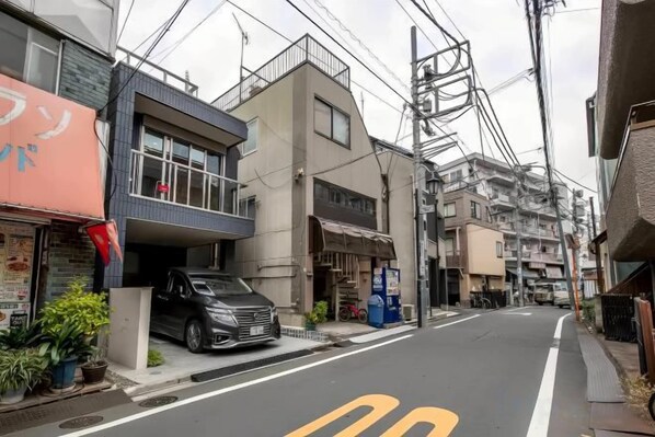 Una calle estrecha en la ciudad flanqueada por edificios, un coche estacionado y cables de electricidad aéreo.