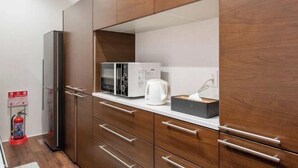 Une cuisine moderne dotée de meubles en bois, d’un réfrigérateur, d’un four à micro-ondes et d’une bouilloire.
