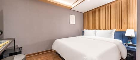 Quarto de hotel com cama, escrivaninha e mesa de cabeceira.