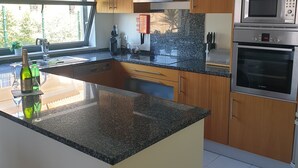 A modern kitchen with granite countertops, wooden cabinets, a Bosch oven, and a built-in microwave. - Wave View Holidays (Albufeira)