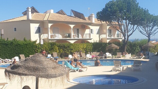 A poolside area with lounge chairs, a small pool, and a building with balconies in the background. - Wave View Holidays (Albufeira)