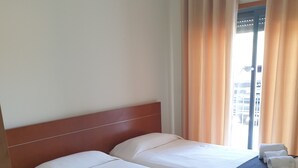 A hotel room with two beds, a wooden headboard, and a view of the city through a window with curtains. - Wave View Holidays (Albufeira)