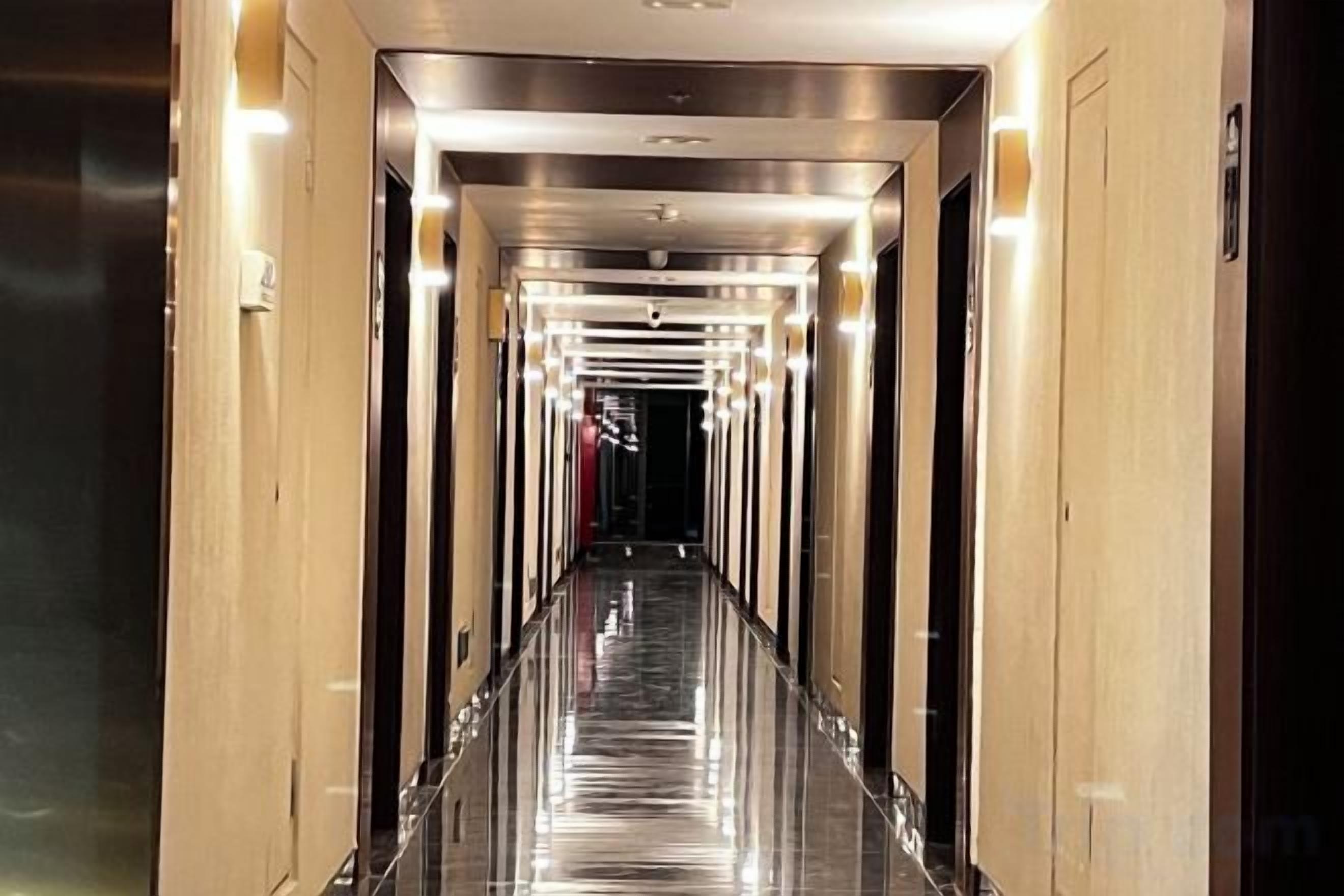 Pasillo de hotel con suelo reflectante, puertas a ambos lados e iluminación superior.