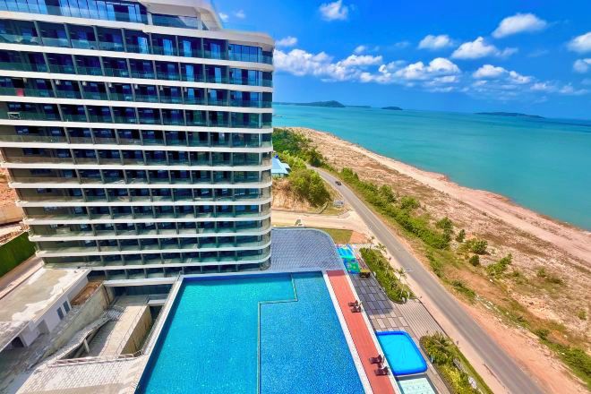 Um hotel moderno com uma piscina grande, vista para o oceano e uma estrada que leva à praia.