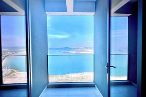 A room with a large glass door leading to a balcony with a view of the sea and distant land. - HC HOTEL (Prey Nob)