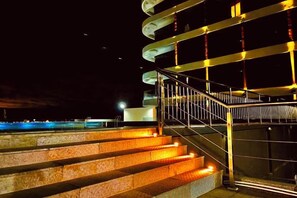 A nighttime view of a spiral staircase with illuminated steps leading to a balcony.