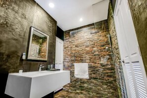 Een moderne badkamer met een stenen muur, een witte wastafel en een handdoek aan een rek.