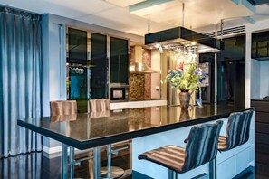 Una cocina moderna con una isla central, taburetes de bar y un comedor con separador de vidrio.