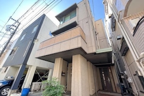 A multi-story residential building with a balcony, a garage, and a small garden area. - Higashikomagata house (Tokyo)