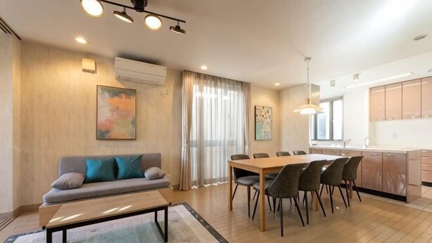 A modern living room with a sofa, dining table, and chairs, a kitchen area, and a large window with curtains. - Higashikomagata house (Tokyo)