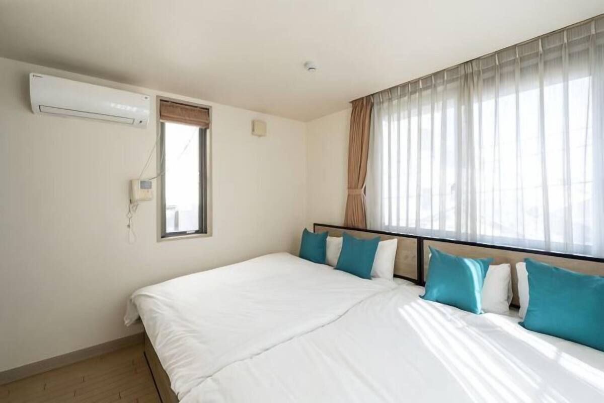 Une chambre d’hôtel équipée d’un lit, d’un appareil de climatisation, d’une fenêtre avec des rideaux et d’un téléphone fixé au mur.