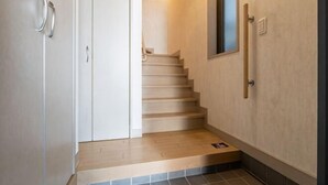 A staircase leading to a landing with a door on the left and a wall-mounted light fixture on the right. - Higashikomagata house (Tokyo)