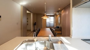A modern kitchen with a central island, a dining area with a long table, and a living space with a sofa and a TV. - Higashikomagata house (Tokyo)