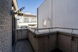 A narrow outdoor corridor with a metal railing, a brick wall, and a tiled floor. - Higashikomagata house (Tokyo)