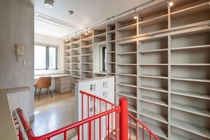 A spacious room with a large built-in shelving unit, a desk, and a red railing. - Higashikomagata house (Tokyo)
