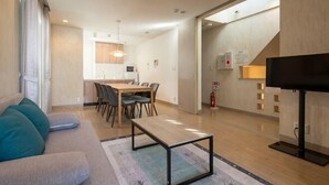 A modern living room with a sofa, a coffee table, a TV, and a dining area with chairs and a table. - Higashikomagata house (Tokyo)