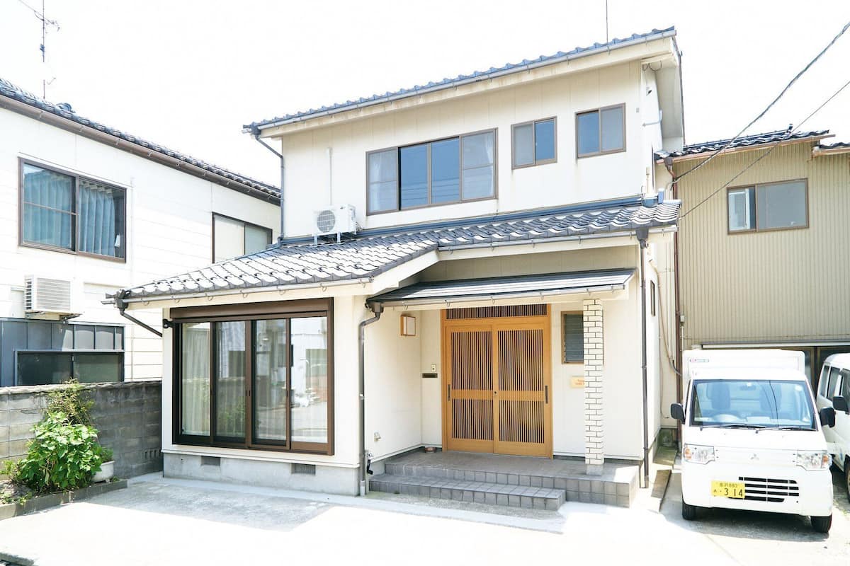 A two-story residential building with a tiled roof, a front entrance with a sliding door, and a small porch area.