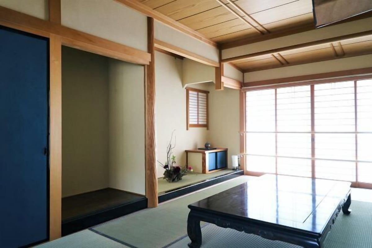 A traditional Japanese room with tatami flooring, a low table, sliding doors, and a window with blinds.