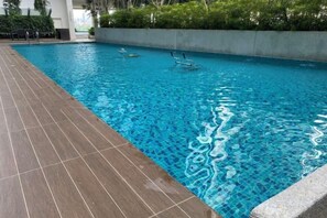 A swimming pool with clear blue water, surrounded by a tiled deck and a low stone wall. - 7Pax Family-Friendly Kepong DesaPark MontKiara (Kuala Lumpur)