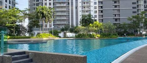 Una piscina rodeada de jardines con escalones que bajan a la piscina, y edificios residenciales altos al fondo.