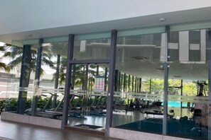 A modern gym with exercise equipment, a swimming pool, and glass walls reflecting the surrounding area. - 7Pax Family-Friendly Kepong DesaPark MontKiara (Kuala Lumpur)
