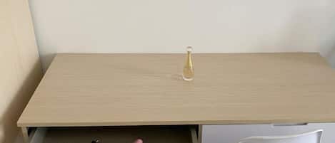 Un escritorio de madera con un cajón, una silla blanca y una pequeña botella sobre la superficie.