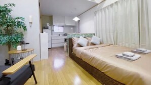 Ein Hotelzimmer mit Bett, Schreibtisch, Stuhl, Pflanze und einer kleinen Küche im Hintergrund.