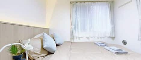 Una habitación de hotel con una cama, una mesita de noche con una planta y una ventana con cortinas.