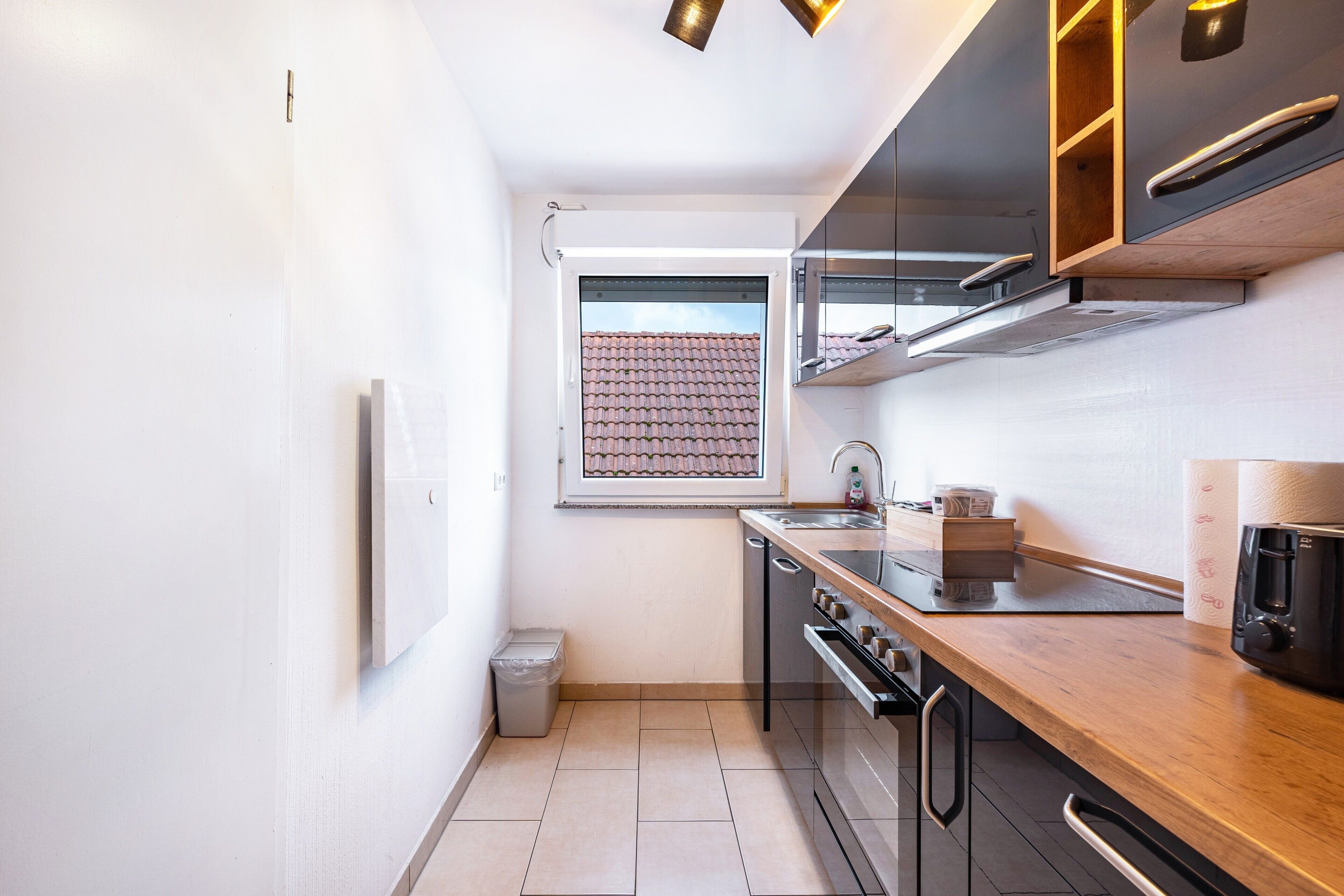 A compact kitchen with a window, a trash bin, and a coffee machine.
