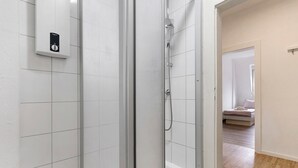 Um chuveiro com divisória de vidro, painel de controle, chuveiro visível e parede revestida com azulejos.