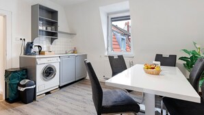 Une cuisine compacte équipée d’un lave-linge, d’une table à manger avec des chaises et offrant une vue par une fenêtre.