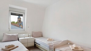 Une chambre avec deux lits, une fenêtre donnant sur un immeuble et une table de chevet avec une lampe.