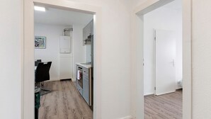 Un couloir mène à une cuisine qui comprend un coin repas, une porte blanche et un tableau encadré accroché au mur.
