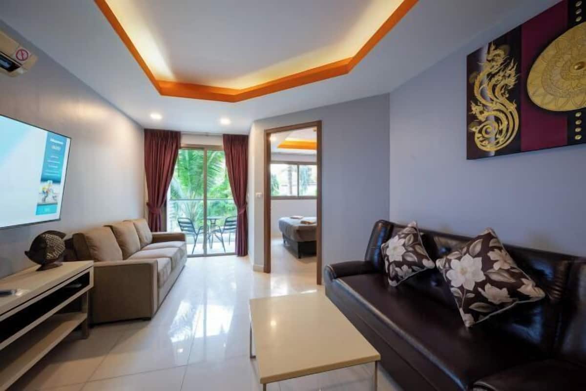 A modern living room with a sofa, a coffee table, and a TV. There is a window with curtains, a door leading to another room, and a decorative wall piece.