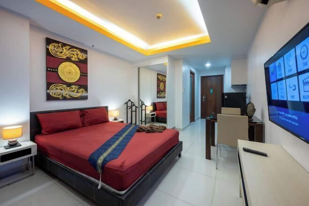 A modern hotel room with a bed, bedside table, TV, and a decorative wall piece.